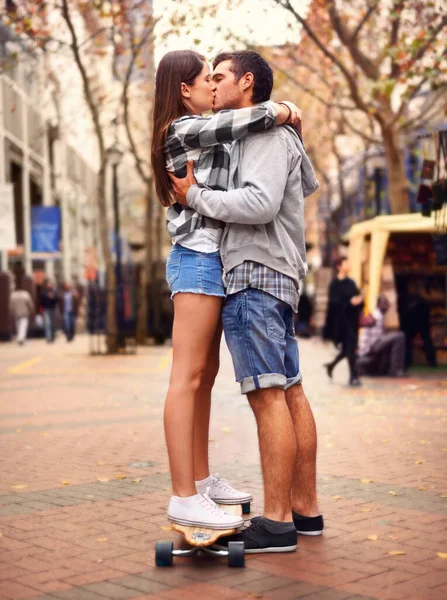 彼女が必要としたステップアップ ダウンタウンの市場でキスを共有する若いスケートボードカップルの完全な長さのショット — ストック写真