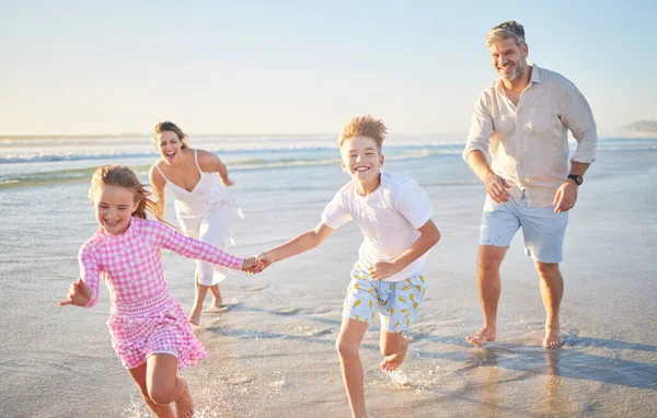 Happy family running on the beach with mother, father and children holding hands for summer holiday, wellness and outdoor development. Mom, dad and kids with healthy fun energy by ocean or sea waves.