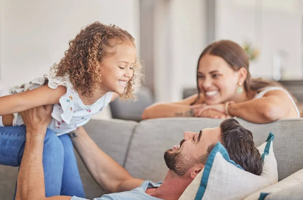 Family, love and support of dad with child playing lifting plane game while feeling happy on the couch in their costa rica home. Smile, joy and fun with man, woman and girl kid or daughter with trust.