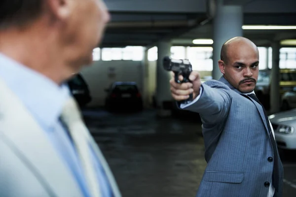 Come with me and come quietly. An angry gangster pointing his handgun at a shocked businessman in a dark parkade