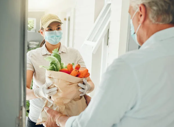 Food delivery, virus and old man in face mask during covid collecting grocery and healthy vegetables at home. Pandemic volunteer giving elderly person groceries at the front door for community work.