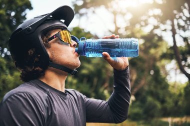Bisikletçi, su ve şişe ormanlarda su, bisiklet ekipmanları ve güneş gözlükleriyle sağlıklı olmak için ağaçların yanında. Egzersiz, egzersiz ya da antrenman yaparken içmek ya da ormanda spor yapmak..