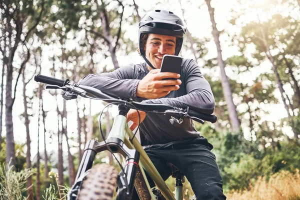 Cyclist, phone and bike happy in forest on ride for fitness, health and wellness. Man, smartphone and bicycle on social media or app for communication while in woods for adventure, workout and sport.