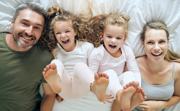 Top view, happy and family with twins in bed smiling together with parents in the morning at home on the weekend. Kids, smile and playful girls enjoy quality time with mother and father on Sunday.