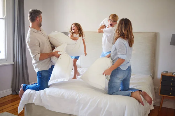 家族の枕の戦いは 両親の寝室で 子供たちは幸せと笑顔 子供たちはベッドに飛び乗り 家でお母さんとお父さんと遊んでいます エネルギーと一緒に狂った楽しさと笑いを持ち — ストック写真