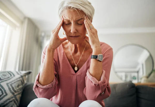 Headache pain, anxiety and senior woman thinking of mental health problem on the living room sofa in house. Sad elderly person with depression, home stress and frustrated with retirement on the couch.