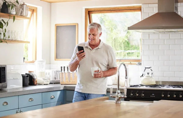 Senior man, morning coffee and phone looking happy while reading text message, online news or browsing internet in kitchen at home. Male using messenger or social media mobile app in Australia house.