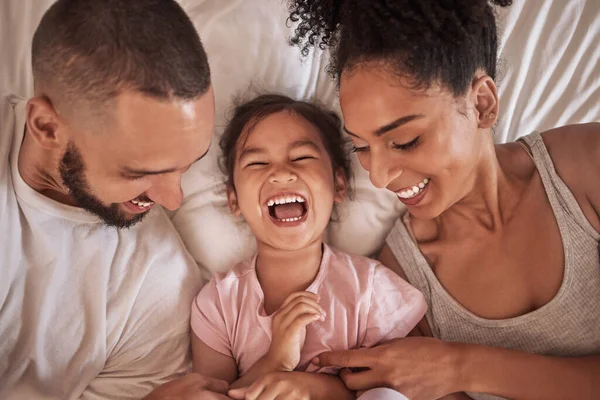Children, family and bedroom with a girl, mother and father laughing, joking or tickling in bed from above. Kids, happy and love with a woman, man and daughter having fun together in their home.