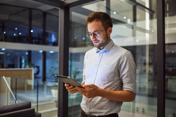 Businessman working on tablet at night for digital marketing online report at the office. Manager or employee reading communication on internet about tech proposal while working late at a startup job.