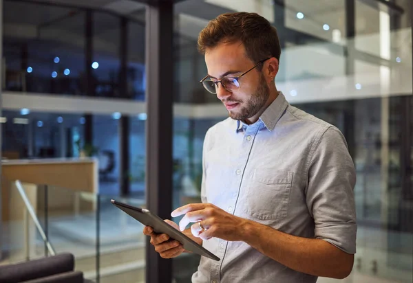 Man in office, working on tablet at night in the office and testing campaign strategy for marketing company. Dedicated professional employee, working late on project and using technology at business.