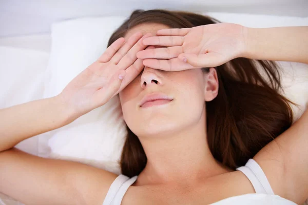 I need more sleep. A young woman lying in bed with her hands over her eyes