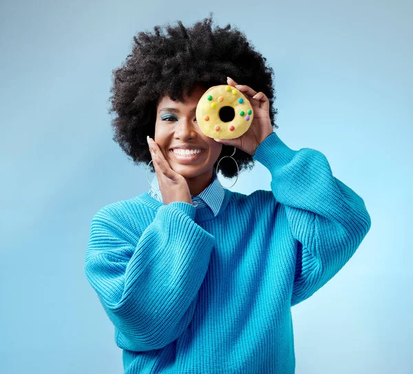 Black woman, smile and donut with blue makeup against studio background. Model, happy and beauty with cake in hand by face show happiness against fashion backdrop with hair, skin and healthy teeth.