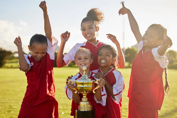 Children, football trophy and winning team of sports competition on soccer field for celebration of goal, win and teamwork after a match outdoors. Youth, kids or girls club after a tournament game.