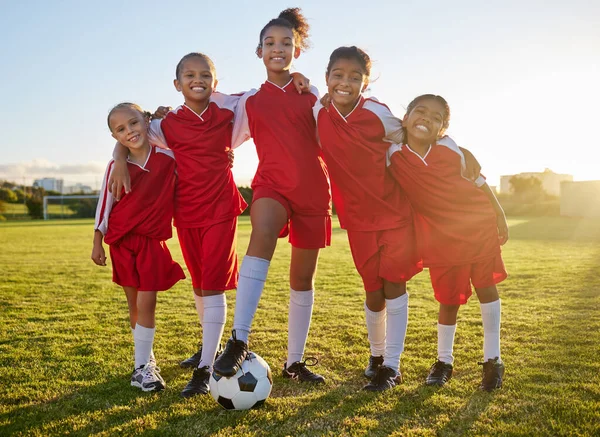 Soccer, team sports and portrait of children training for football game on a grass field together. Happy, smile and young group of girl athletes in partnership and teamwork for sport match at school.