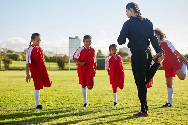 Team, soccer and girls stretching in football stadium with coach in training, sports and group warm up together. Healthy, teamwork and young school children doing exercise with fitness instructor.