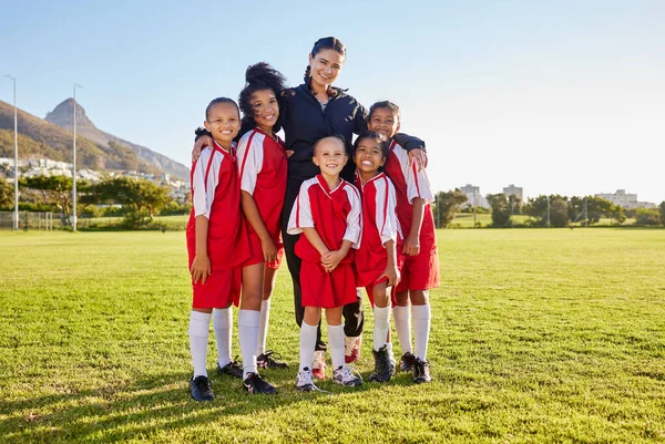 Team, soccer and coach smile on field together in portrait after training, game or workout in sun. Football, girl and woman with diversity in happy sports group on grass for teamwork in Cape Town.