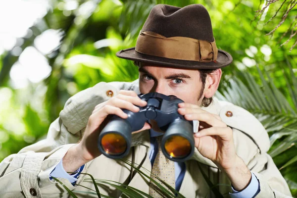 He doesnt miss a thing. Private investigator using binoculars to spy on someone from the bushes