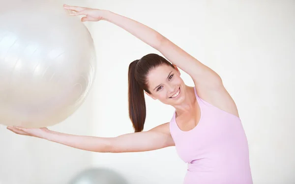 Working every muscle. an attractive young woman with her arms stretched above her head holding an exercise ball