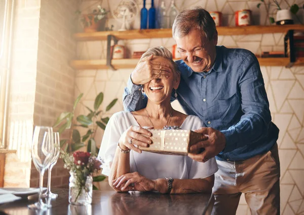 Gift, surprise and senior couple in restaurant for retirement celebration or happy birthday with wine glass, present and roses. Elderly woman with marriage anniversary event with vintage fine dining.