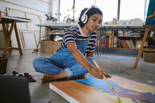 Music, painting and art with woman on floor of workshop studio working on creative, idea or vision on canvas. Relax, designer and goals with girl artist and headphones for peace, wellness or freedom.