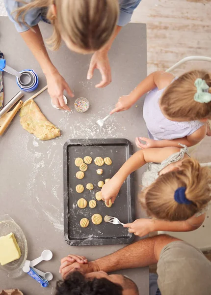 Baking, family and girl children learning to bake cookies in kitchen at home from above with mom, dad and sister. Man, woman and kids having fun with dough, cooking and food together making pastry.