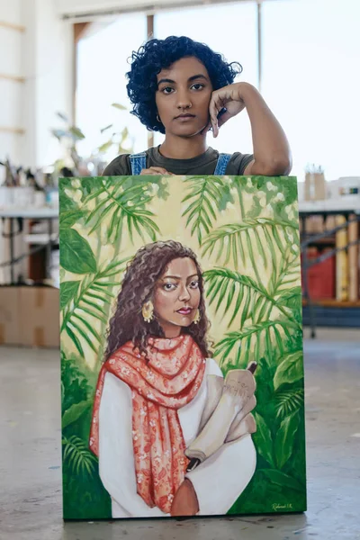 Portrait, painter and woman with creative painting on canvas in art gallery or studio after working with watercolor palette. Talent, and young Indian artistic student with creativity in workshop.