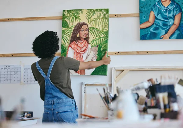 Woman artist, painter and hanging canvas on wall for exhibition to display in studio, art gallery or workshop. Female, lady and creative showing and holding artistic piece and painting in workspace