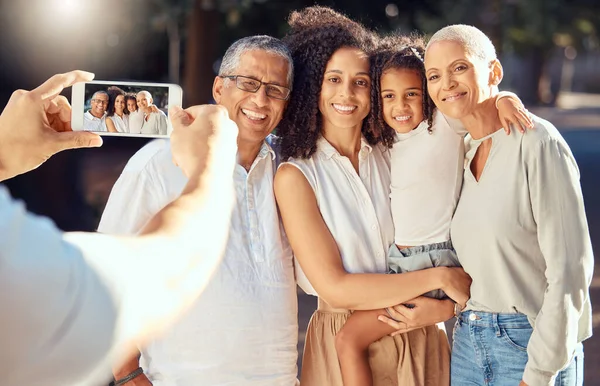 Phone, screen and happy family relax and smile while posing for a picture outdoors together, loving and embracing. Child, mother and grandparents bonding on a trip in nature, hug and enjoy summer.