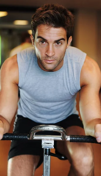 Focused on moving forward in fitness. A handsome young man wearing sport clothing and using a exercise bike at the gym