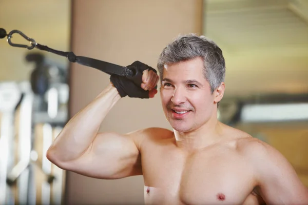 Effort at the gym. A shirtless man working out his biceps at the gym