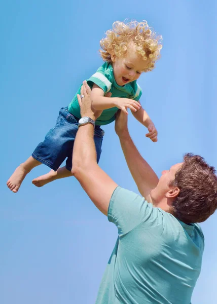 Szórakoztató Apa Egy Apa Lengeti Kisfiát Levegőben Egy Égi Háttérben — Stock Fotó