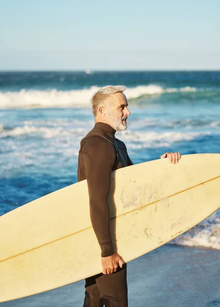 Senior man, beach and surfboard surfer, ready to surf Australia sea waves on vacation or holiday. Health, fitness and elderly retired male rest after surfing, training or recreation exercise in ocean.