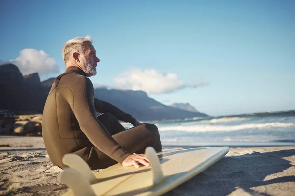 Surfer, surfboard and senior man on beach for surfing adventure trip waiting for sea waves in nature for water sports activity. Fit male at ocean in summer for surf training on travel in South Africa.