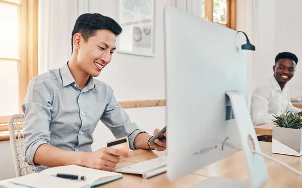 Credit card, online payment and businessman shopping on mobile app on a phone in an office at work. Asian employee banking with debit card on smartphone, happy with retail and finance on the web.