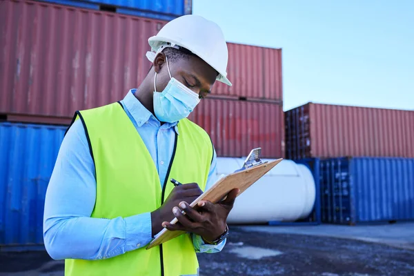 Black man working in covid with face mask, shipping container in supply chain industry and logistics stock inventory. Healthcare safety in export company, essential worker in port and medical virus.