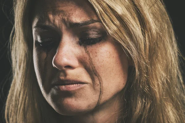 Sad, depression and woman crying on dark studio background for mental health or psychology awareness. Young, depressed mental illness person tears and smudge makeup for anxiety, violence or fear.