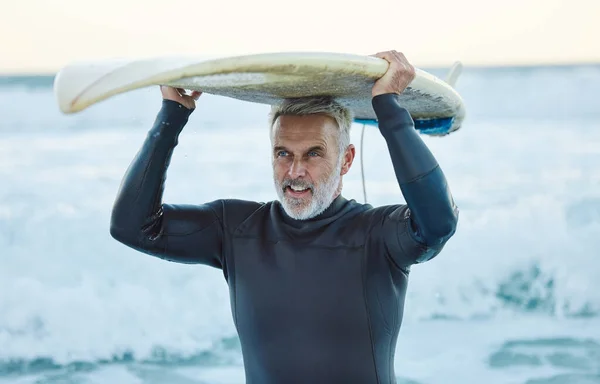 Senior man, ocean surfer and carrying surfboard on holiday, vacation or summer trip in Canada. Workout, fitness and retired male with board after surfing, water sports and training exercise by sea
