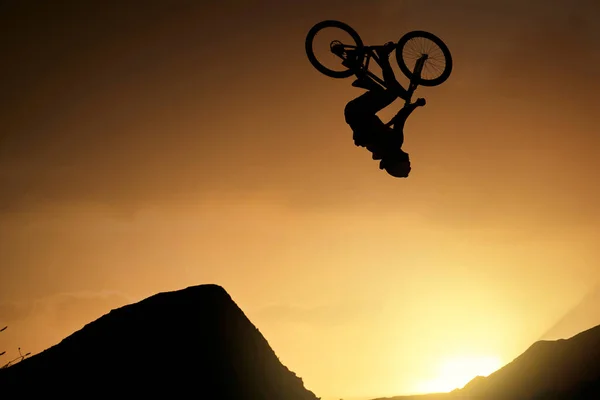 Cyclist, fitness and stunt jump at sunset in Colorado countryside nature mountains in fitness, exercise or training. Danger risk, extreme sports mountain bike or freedom man in sunrise energy workout.
