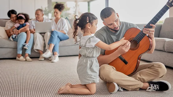 Father, child and guitar teaching, learning or music in the living room with family in the background. Girl and man play with a musical instrument together bonding in the house with creative hobby.