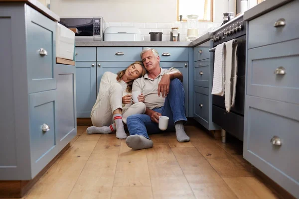 Coffee breakfast, relax and senior couple with smile on the kitchen floor in the morning in their house. Calm elderly man and woman in retirement talking with tea and love in marriage in home.