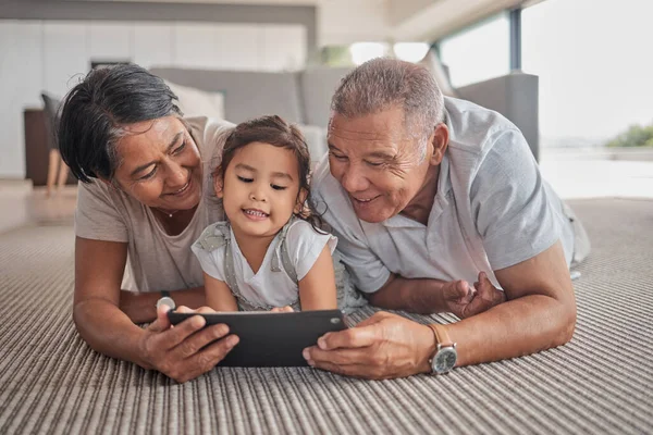 Relax, grandparents and cartoon on tablet with child on home floor together in the Philippines. Filipino family bonding time with grandfather, grandmother and grandchild watching animation online