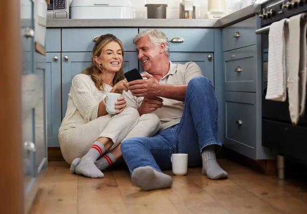 Senior couple, phone or bonding with morning coffee on house or home hotel kitchen floor in trust, love or security. Smile, happy or technology for retirement elderly man and woman with internet news.