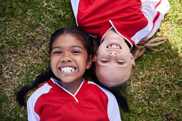 Soccer, sports and children with girl friends lying on a grass field during a football game or match. Kids, training and health with a female child and friend on a pitch for team sport from above.