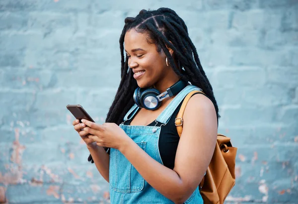 Black woman, smile and phone in social media with headphones in joy for 5G  connection in the outdoors. Happy African American female student smiling  for technology and internet on mobile smartphone