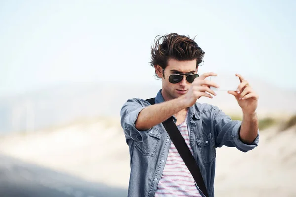 stock image Preserving some memories of my trip. Trendy young man standing on the road and taking a picture on his phone