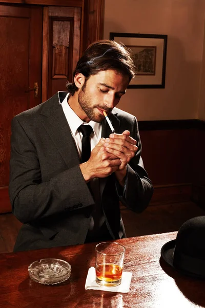 Just taking it easy. Portrait of a well-dressed young man sitting at a bar with a drink and a smoke