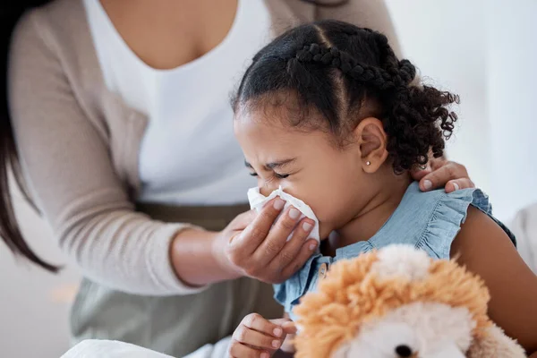 Mother clean sick child nose with tissue, playing with toy or teddy bear in bedroom at family home. Teacher at kindergarten use toilet paper, to help clean young girl face after sneeze or runny nose.