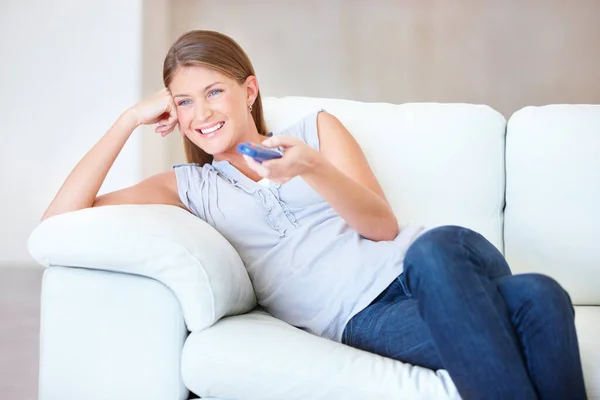 这是伟大的表演 微笑的年轻女子一边在电视上欣赏节目 一边在沙发上放松 — 图库照片