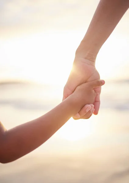 Closeup of unknown mixed race mother holding her little son or daughters hand while bonding together on the beach at sunset. Hispanic child showing trust in single mother. Loving and caring parent.