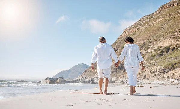 Rear view of a Mixed race senior couple taking a romantic walk on the beach and holding hands on a sunny summer day outdoors.